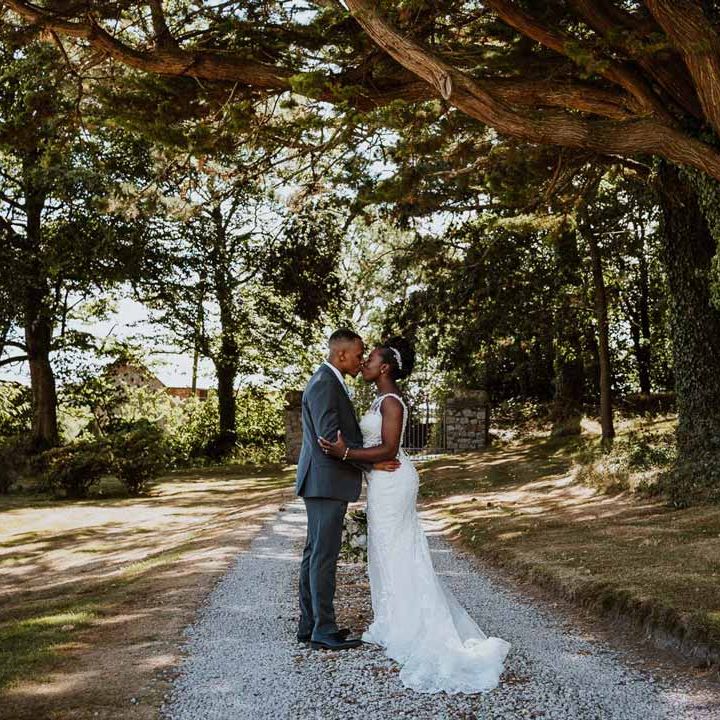 Groom in charcoal grey grooms suit, light grey patterned waistcoat and light grey patterned tie kissing bride in lace and mesh boatneck wedding dress with silver bridal hair accessories