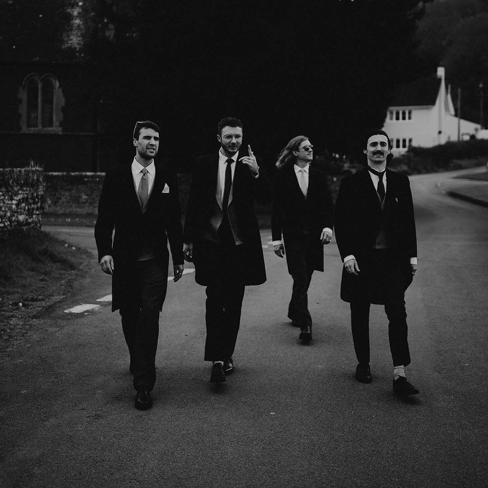 The groomsmen walk together like a boy band in morning suits 