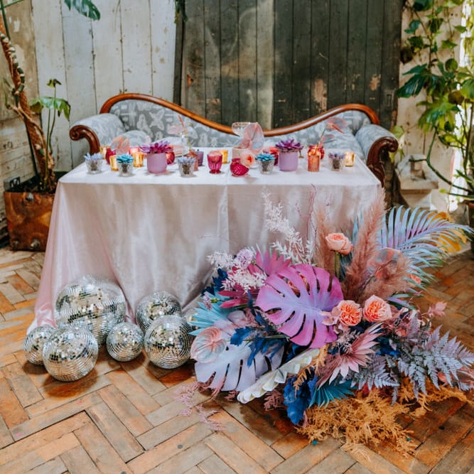 Colourful sweetheart table with iridescent flowers, disco balls and votives. 