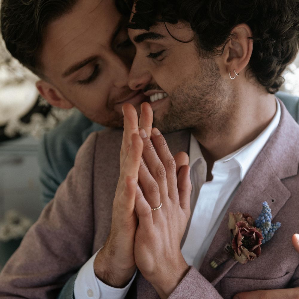 Grooms sit together whilst clasping hands together on wedding day
