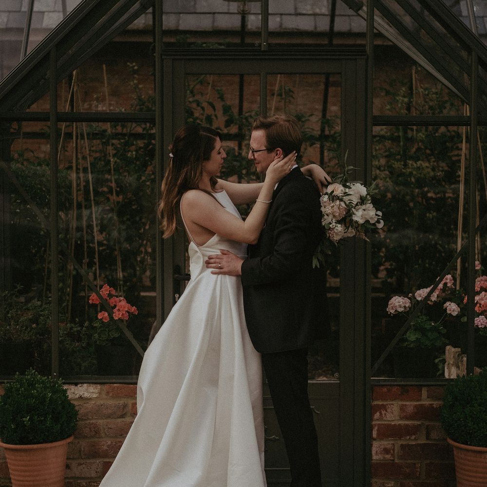 Bride & groom embrace outside greenhouse on their wedding day at Elmore Court