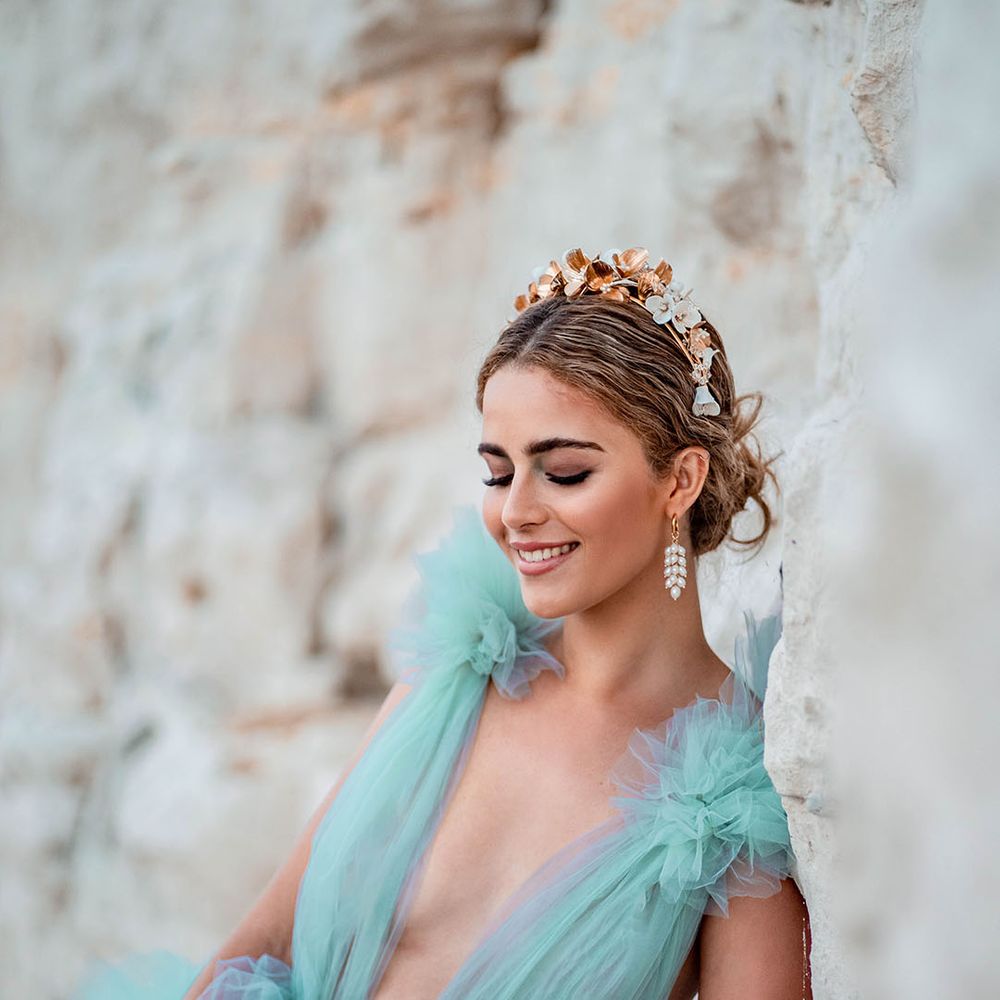 Groom with a pinned up do wearing a gold headband and dangly earrings wearing a Millia London green tulle wedding dress 