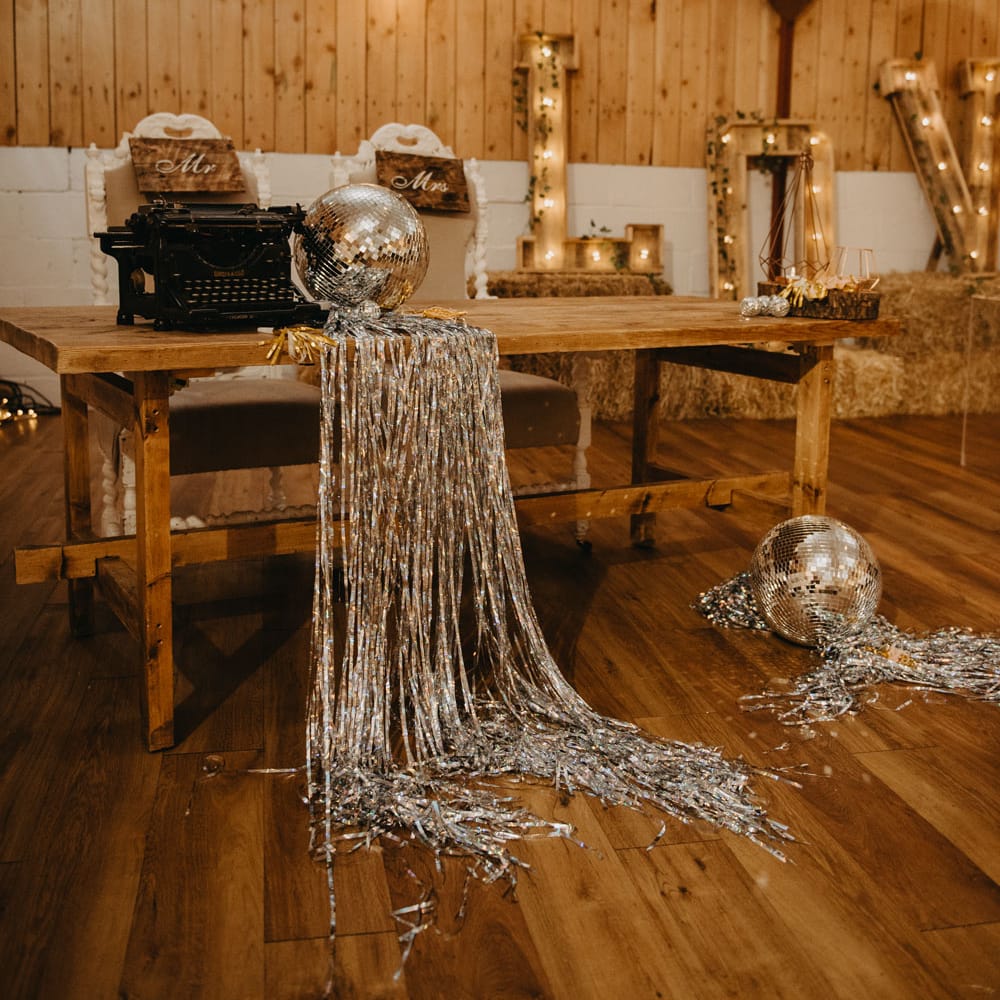 Wooden table with large wooden letters, fairy lights, disco ball and streamers for rustic wedding reception