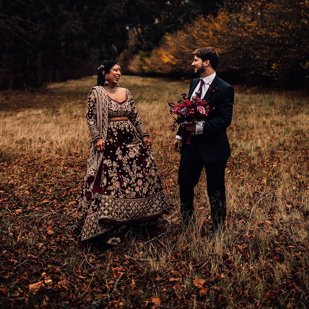 Bride wears Indian Saree wedding dress and matches in groom in dark suit holding stunning a mixture of dark & hot pink flower bouquet 