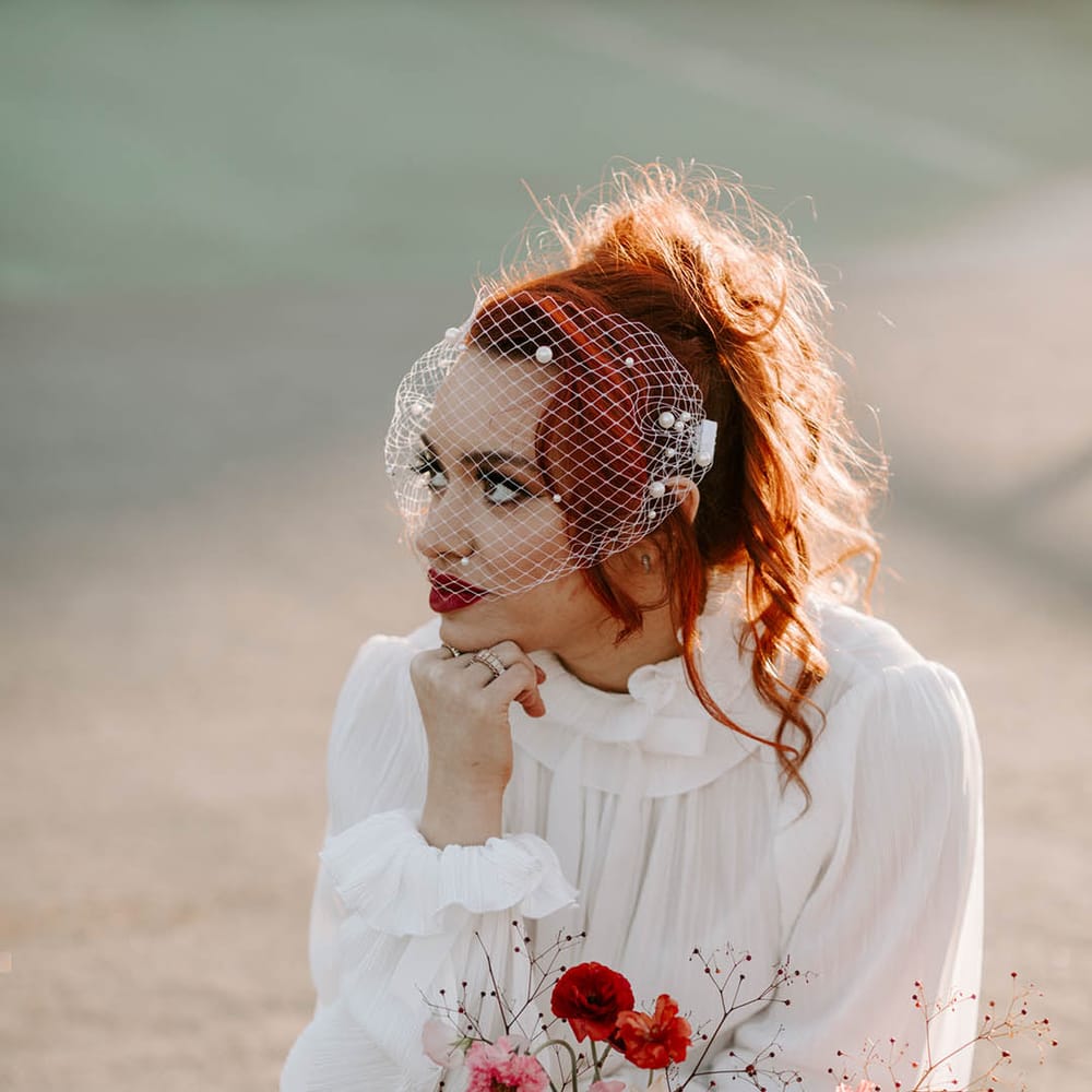 Bride in a short wedding dress and birdcage veil holding a red and pink wedding boquet with sweet peas and butterfly ranunculus 