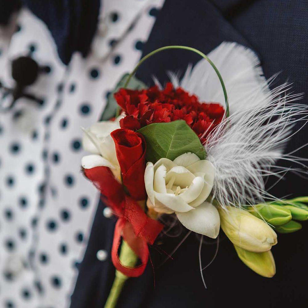 White and red floral buttonhole complete with feather