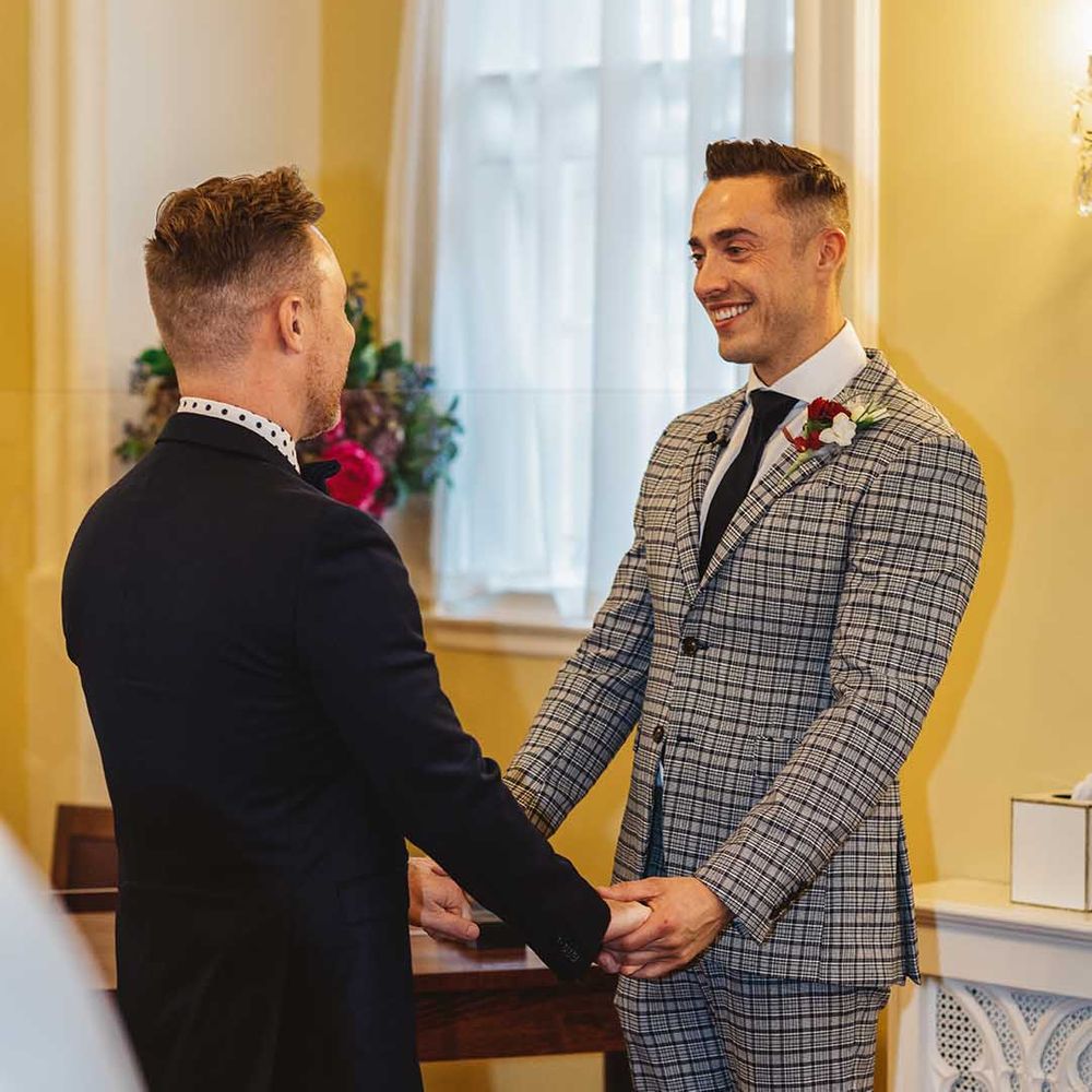 Grooms hold hands during wedding ceremony