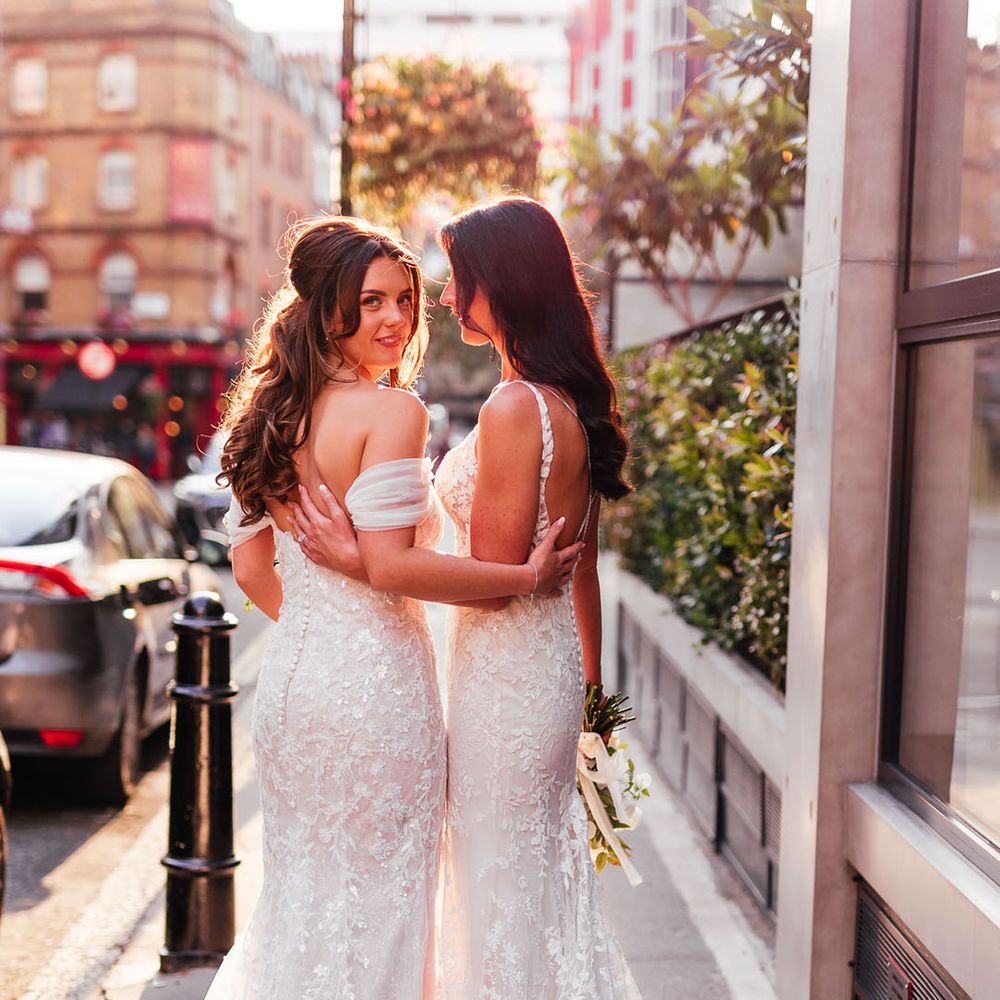 Two brides in lace wedding dresses arm in arm at their urban London wedding 