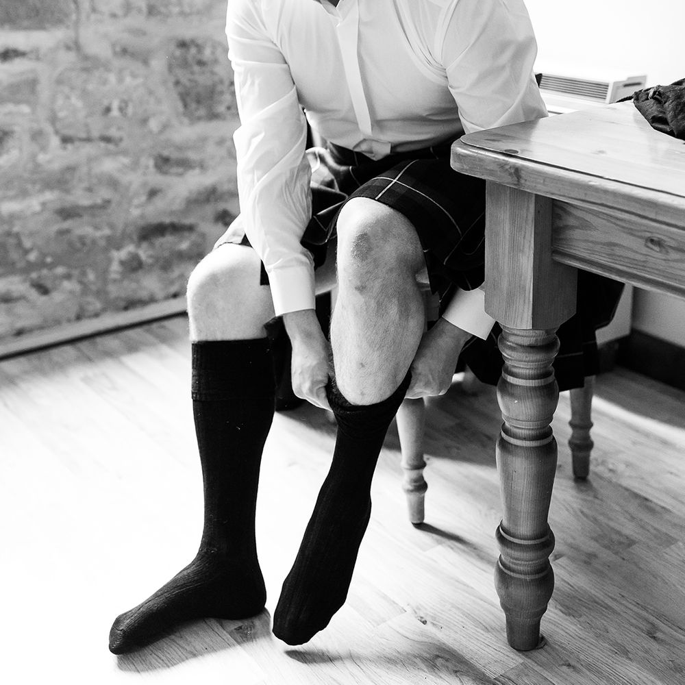 Groom gets ready for his wedding day as he puts his socks on for the big day 