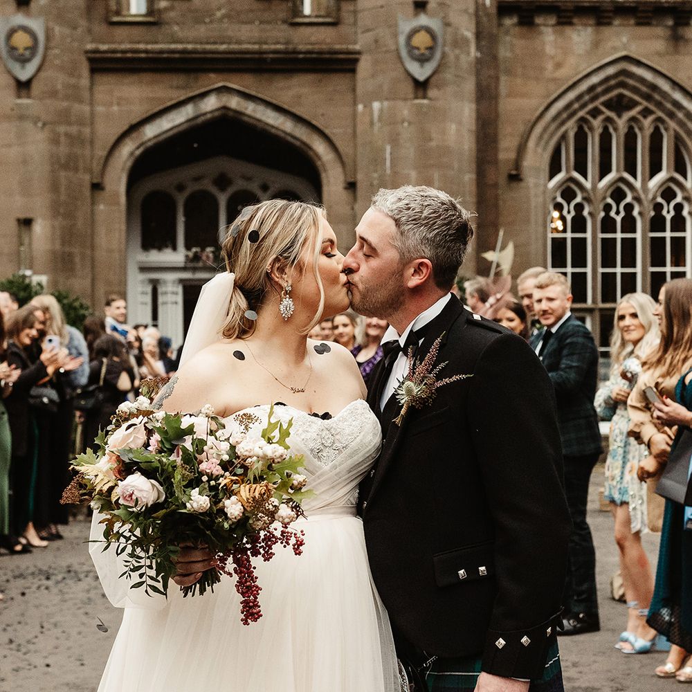 Bride and groom share a kiss outside Drumtochty Castle wedding venue with black circle confetti