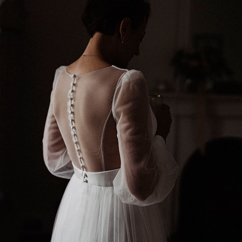 Bride in sheer back and long sleeve wedding dress from Sassi Holford with button detail and a tulle skirt