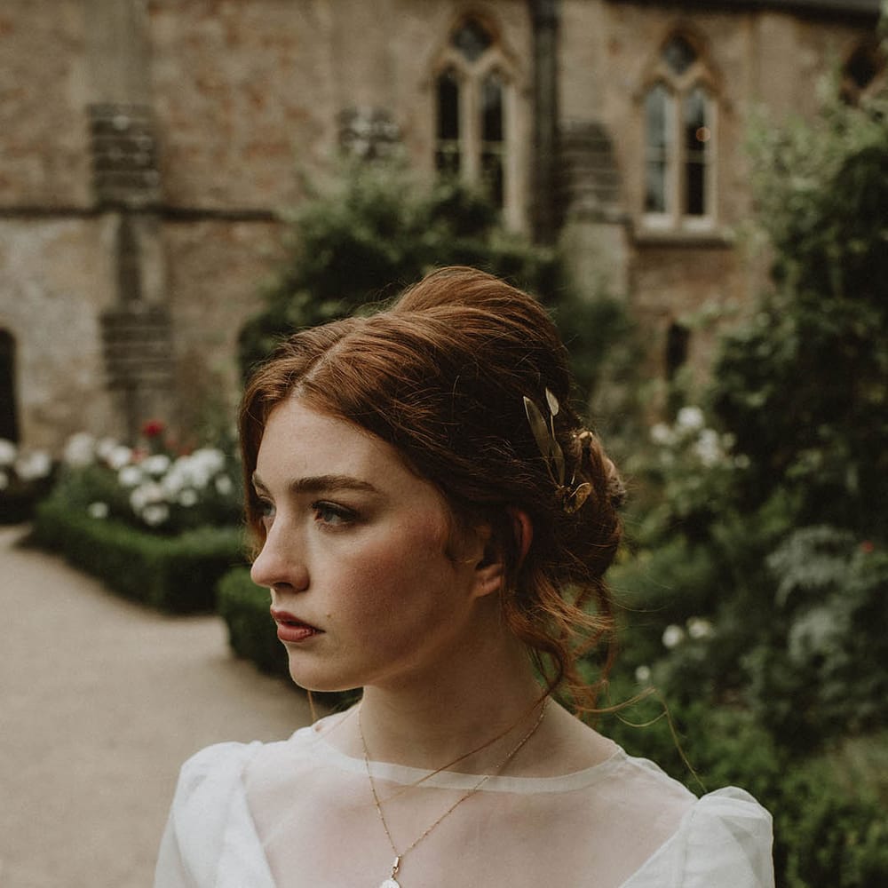 Bride with natural makeup wearing a wedding dress with sheer top layer and delicate gold necklace 