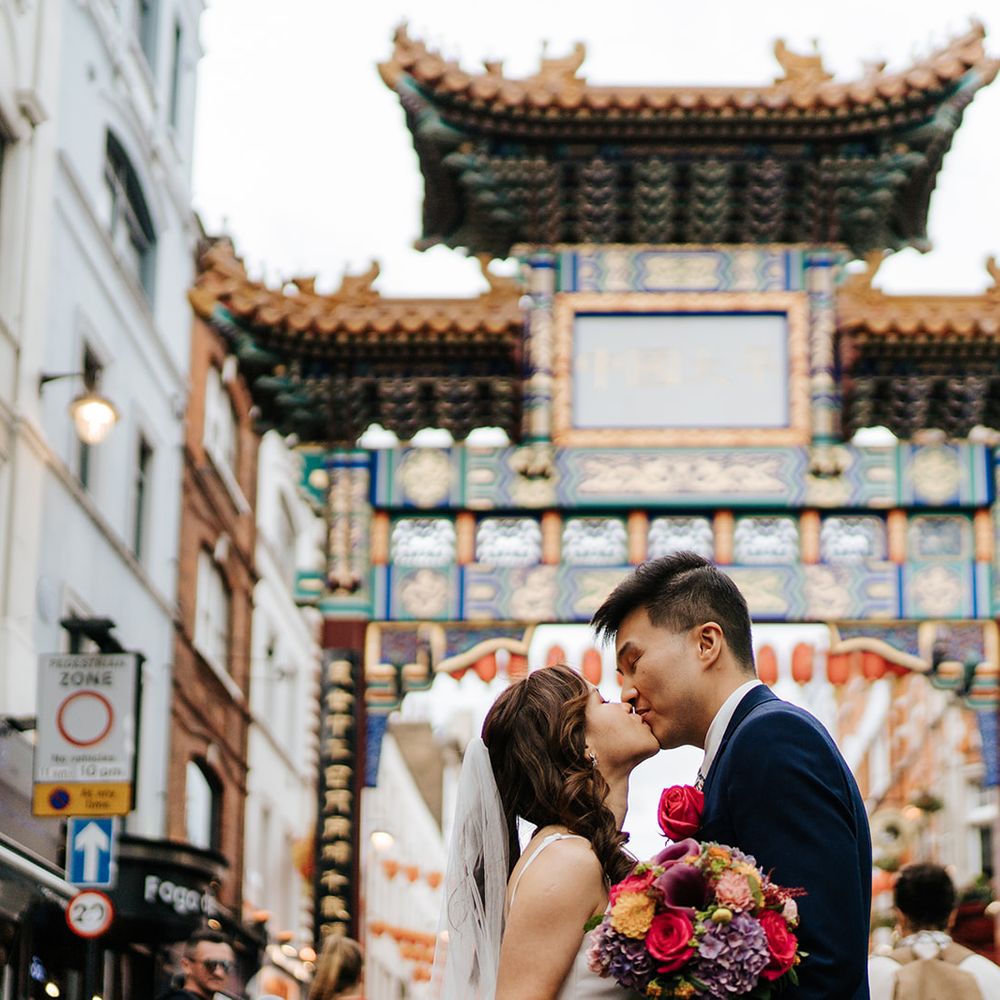 Bride & groom look lovingly at one another in China Town in London on their wedding day after taking London bus
