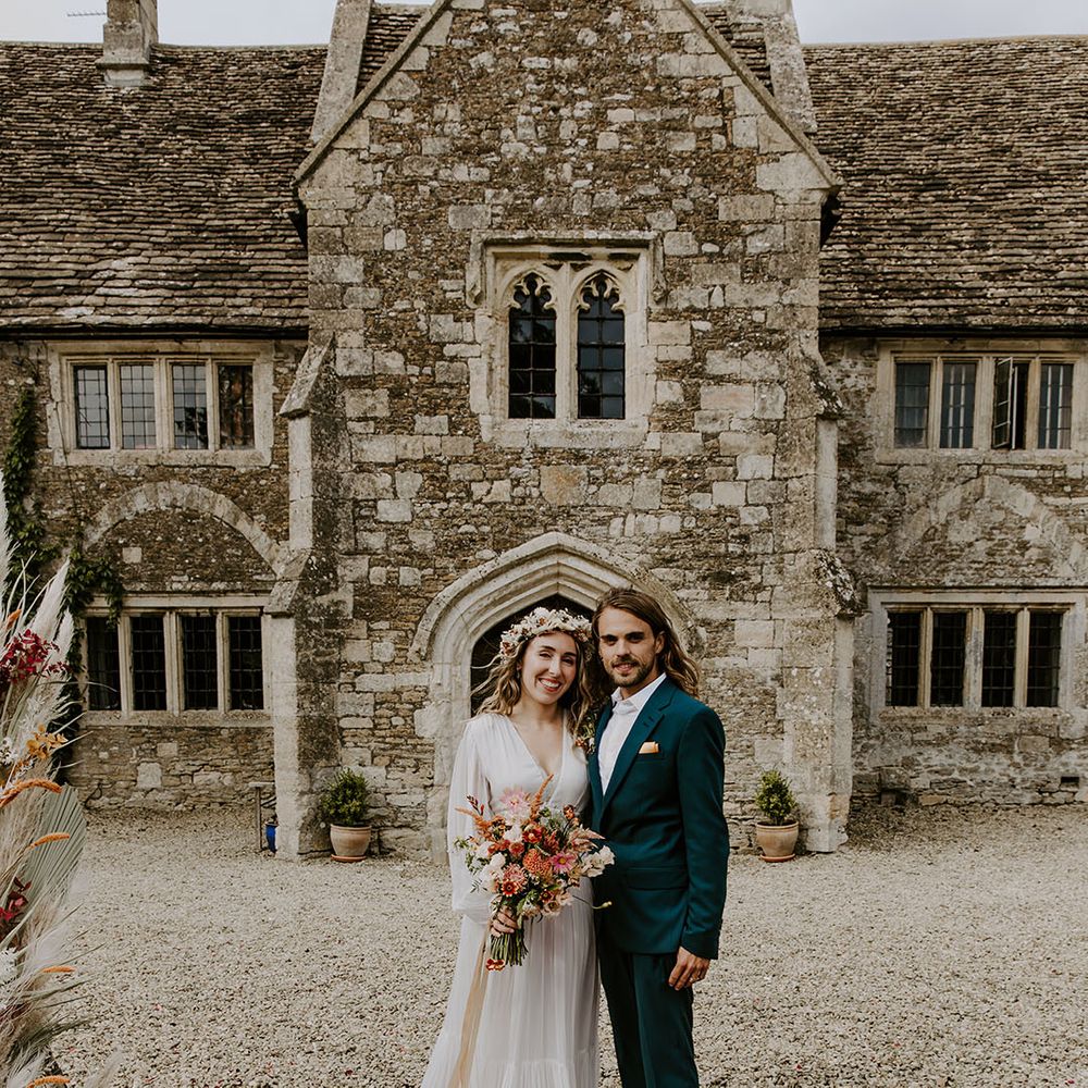 Bride holds colourful floral bouquet and stands with her groom in front of Moroccan styled rug outdoors
