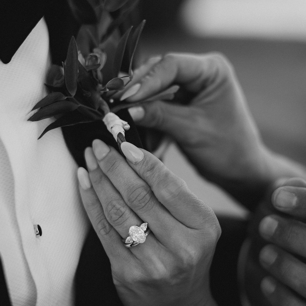 Bride helps pin her grooms floral buttonhole in black & white image