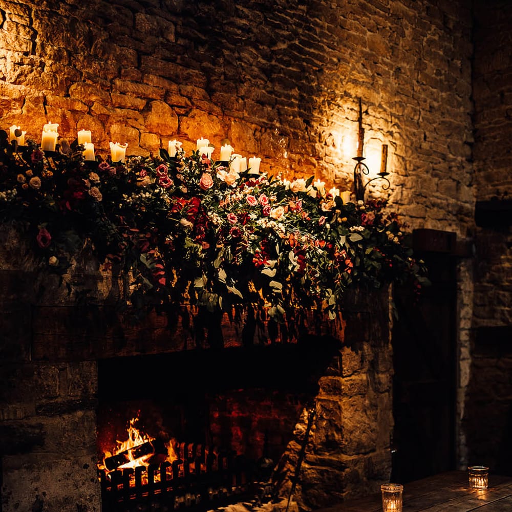 Cripps Barn wedding venue with a roaring fire and soft candlelight with pretty pink flowers