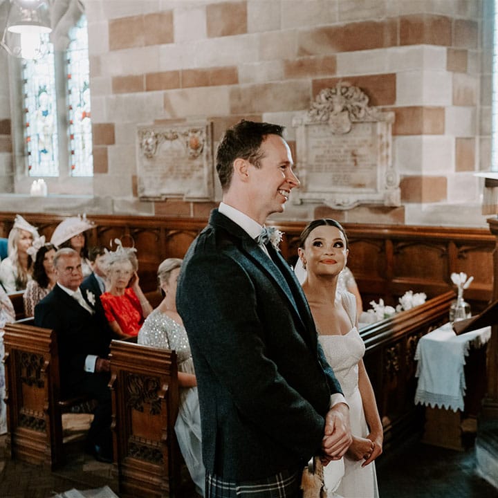 Bride looks lovingly up at the groom as they stand together at the altar with the groom in a kilt for church ceremony 