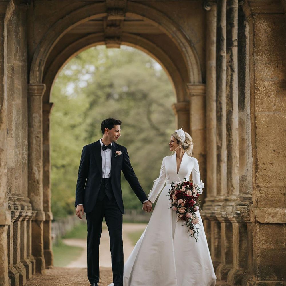 Bride in a collared long sleeve Jesus Peiro wedding dress walking with the groom in black tie for their Bridgerton inspired wedding at Stowe House