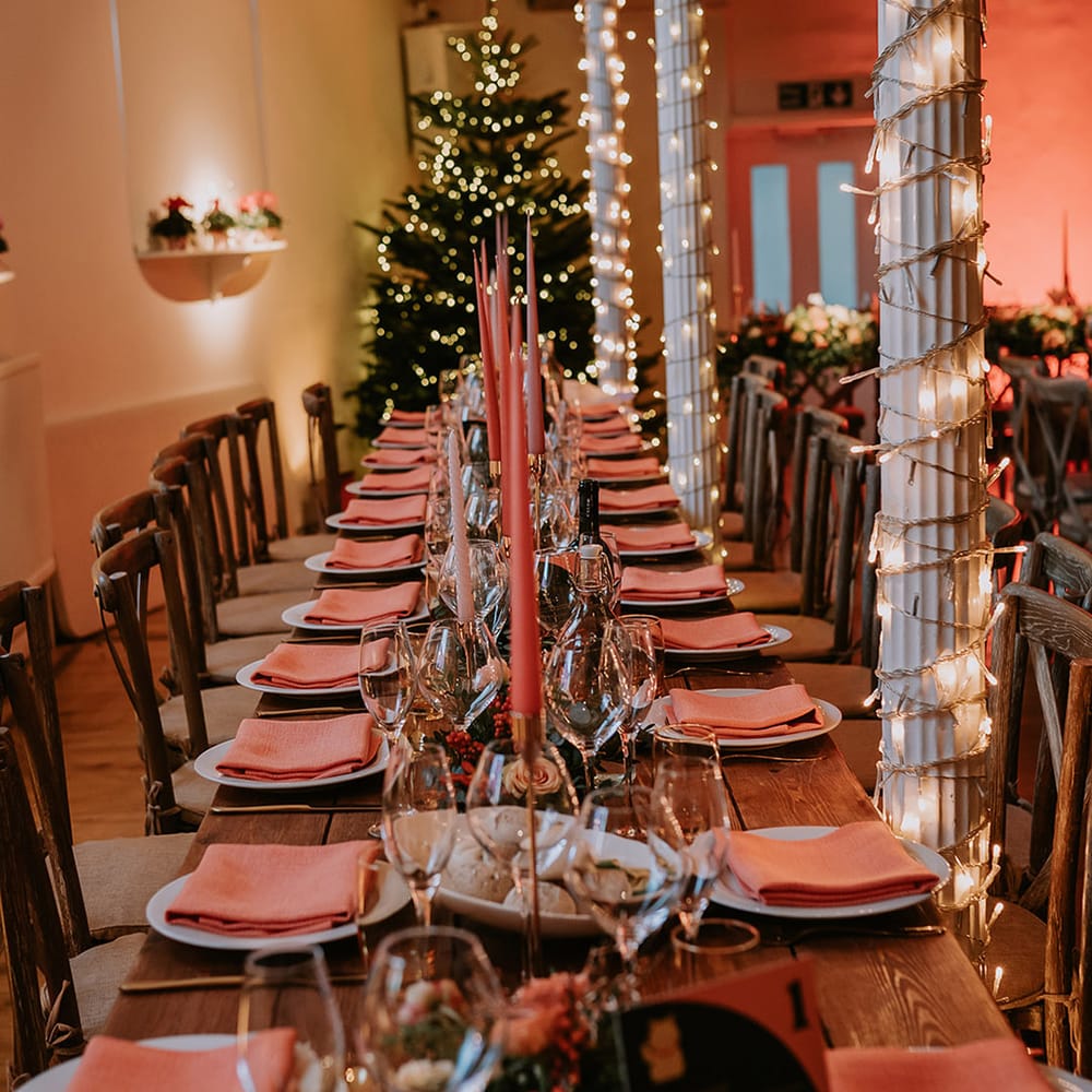 Neutral Christmas inspired tablescape with orange napkins, orange tapered candles, gold candlestick holders, a large Christmas tree and fairy lights 