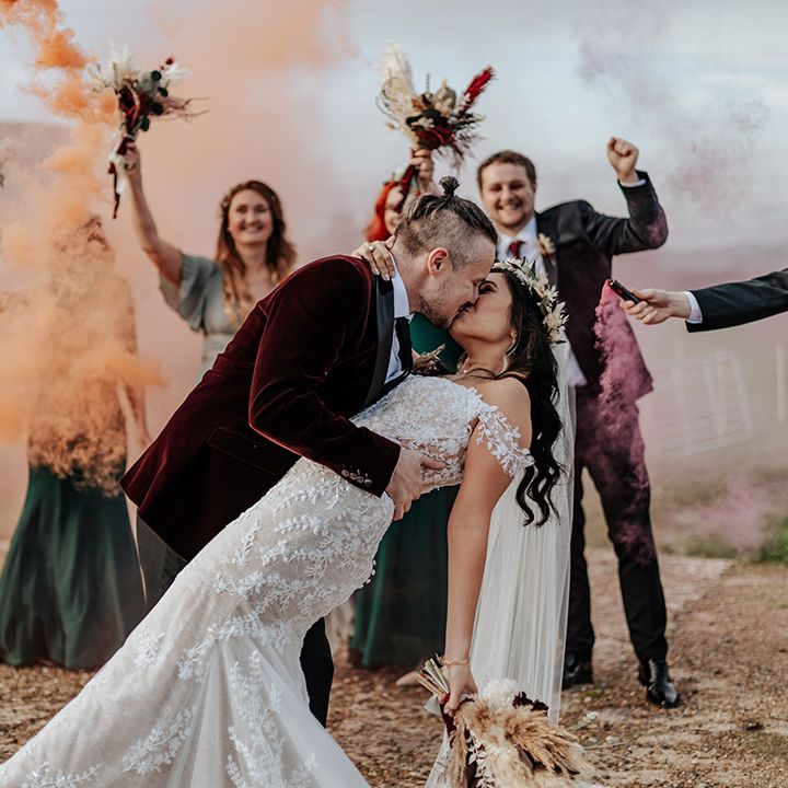 Smoke bomb wedding photoshoot with the groom tipping the bride back and giving her a kiss 