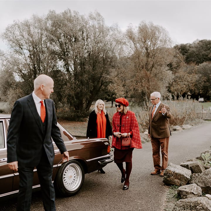 The wedding guests in red, brown, and orange autumnal theme wedding outfits arrive at the church for the wedding 