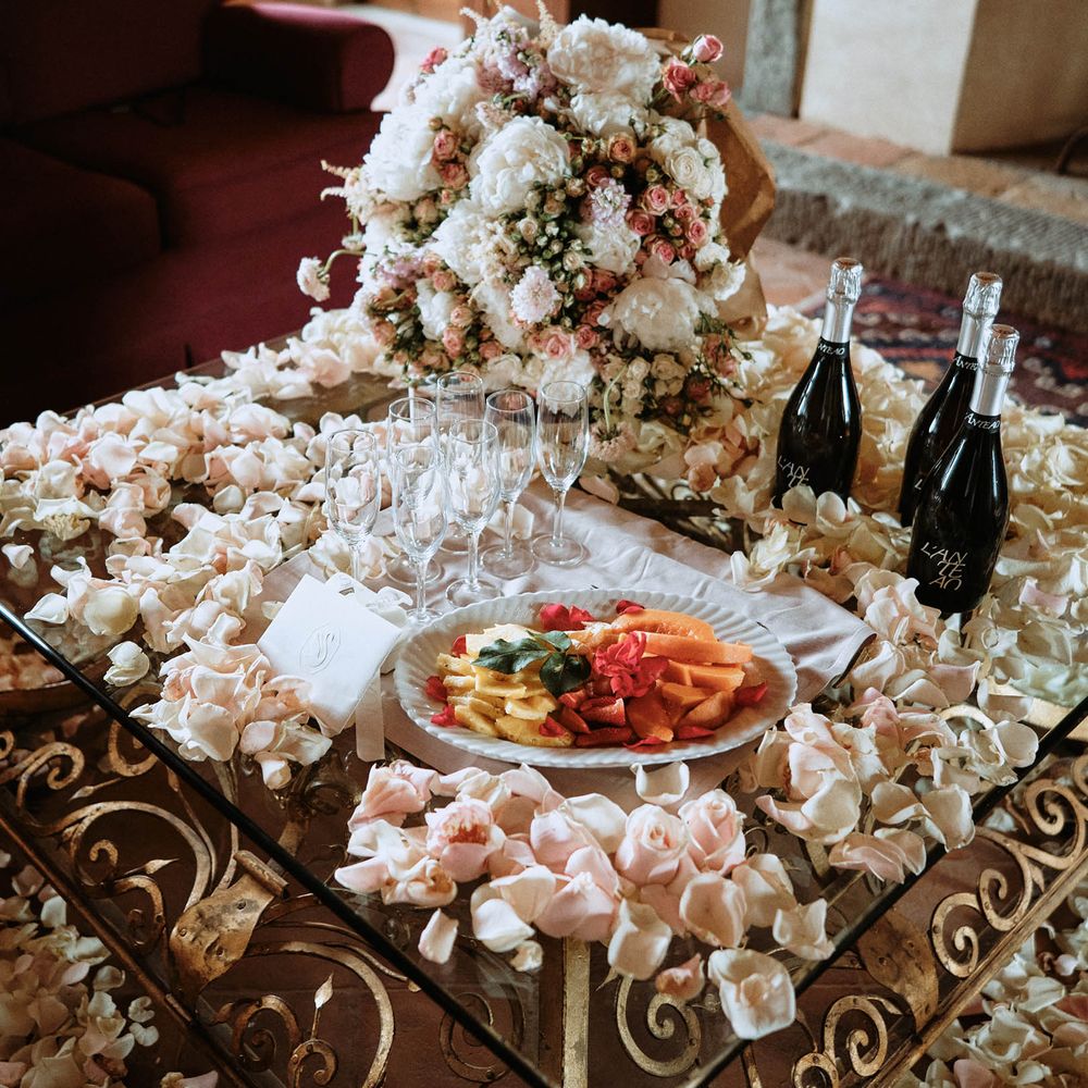 Fruit platter and prosecco surroundeed by pastel pink petals and white roses on the morning off the wedding