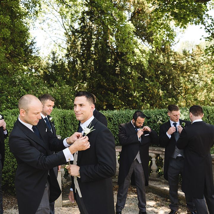 The groom and groomsmen all put on their white rose buttonholes for the classic country house wedding 