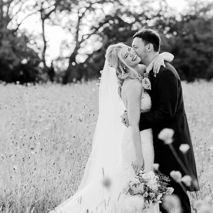 The groom kisses the bride on the cheek as she laughs for their cute couple wedding photos 