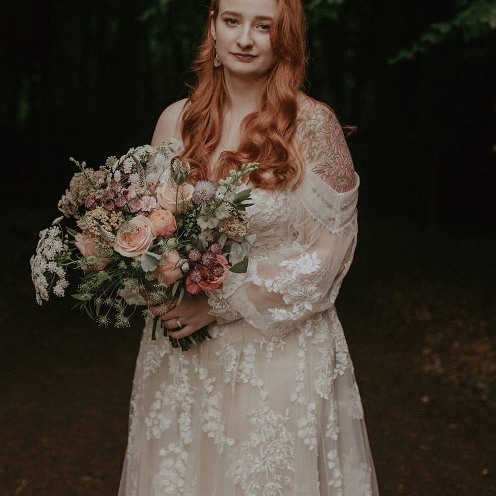 Bride in off the shoulder boho floral lace wedding dress holding pink flower bouquet 