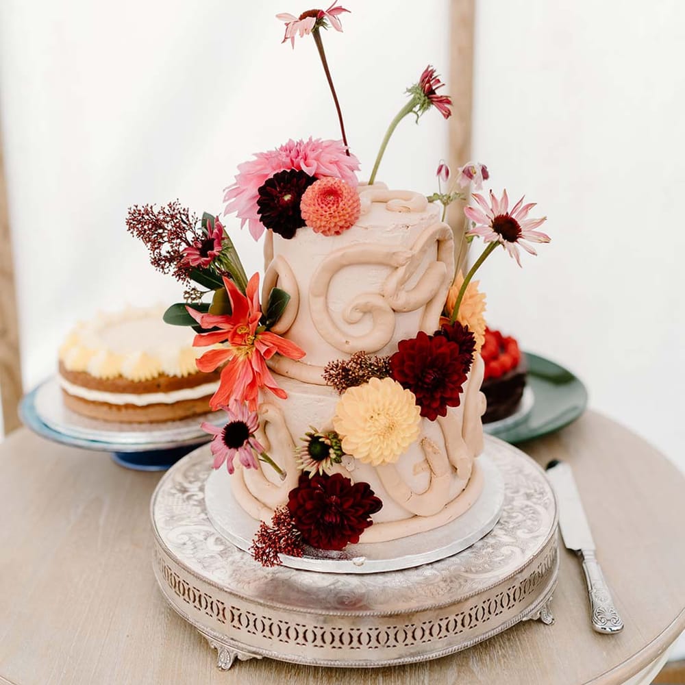 Small two tier off white wedding cake with icing details and colourful edible flower decorations 