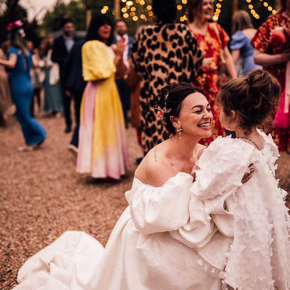 A flower girl in a butterfly gown with matching butterfly accessories hugging the bride 