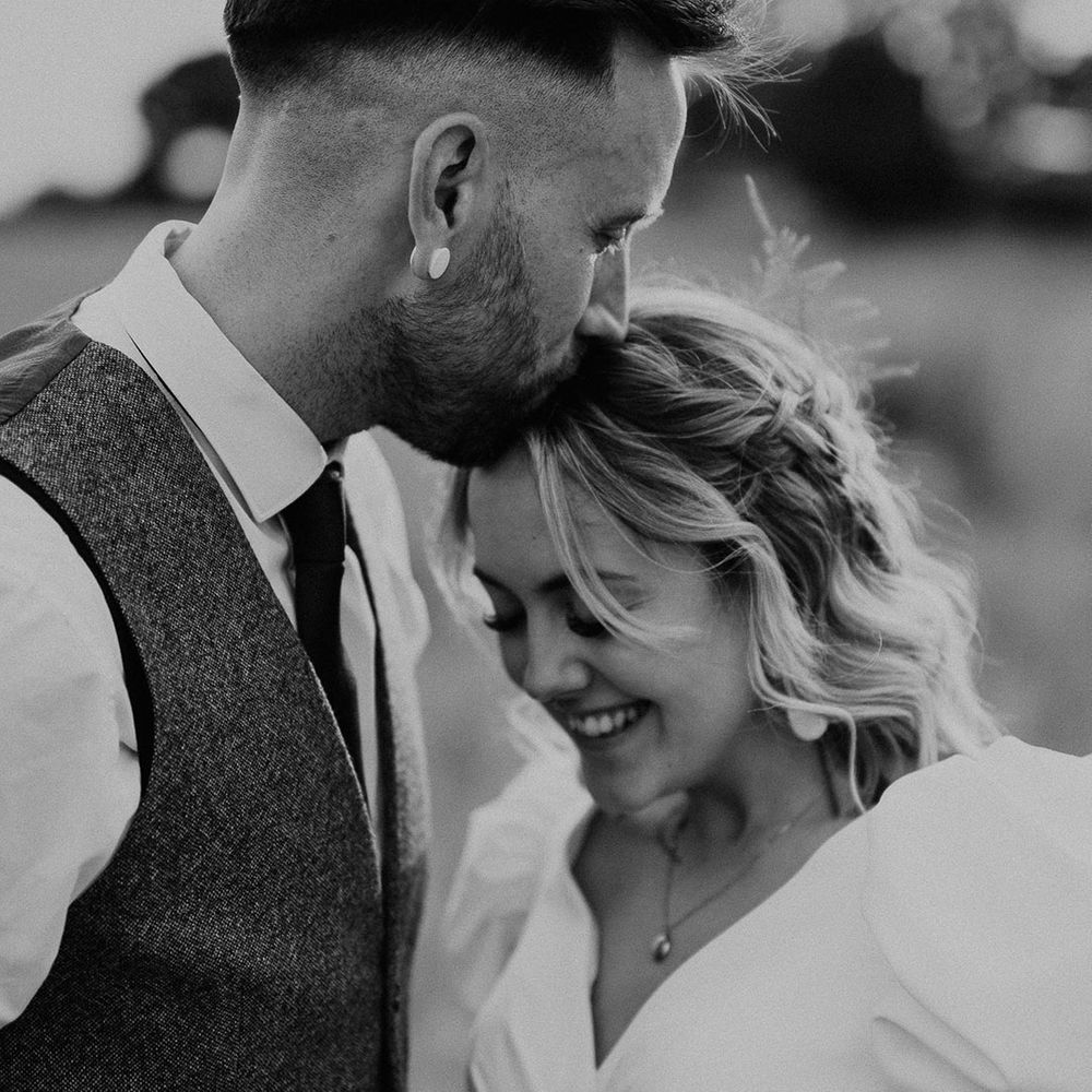 The groom kisses the bride on the head at their rustic festival wedding 
