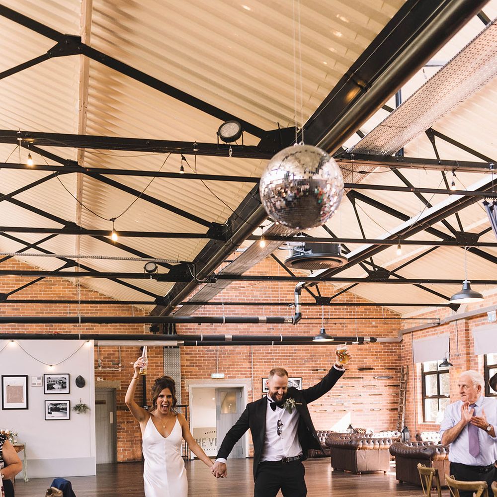 The bride and groom enter their wedding reception together with beer in hand 
