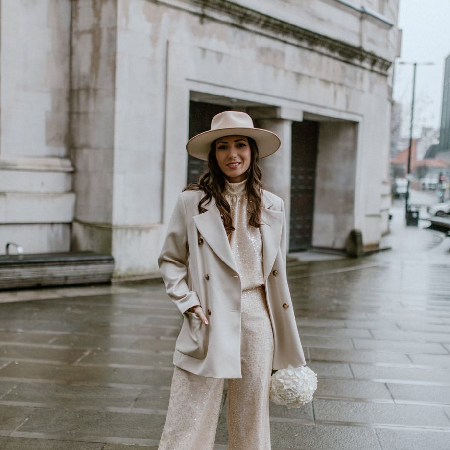 City bride in sequin trousers and top with complementing neutral coat and hat 