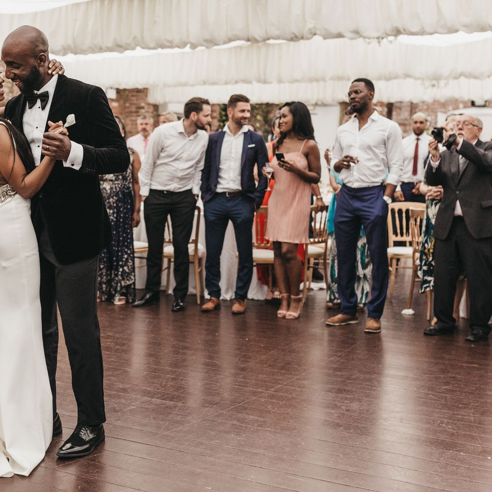 Wedding first dance with the Black groom in a velvet jacket leading his bride in a backless fitted wedding dress with low back detail 