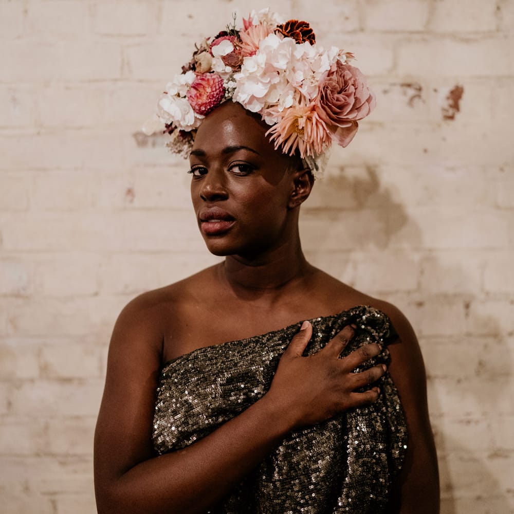 Black bride with alopecia wrapped in a black shimmering cape and wearing a pink floral headdress 
