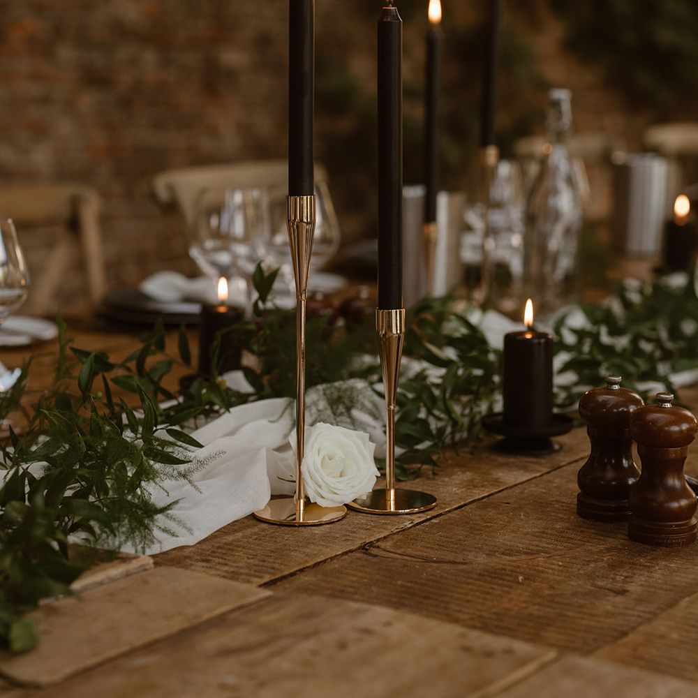Tall black candles in golden candlesticks for rustic wedding table decor with greenery and white rose details