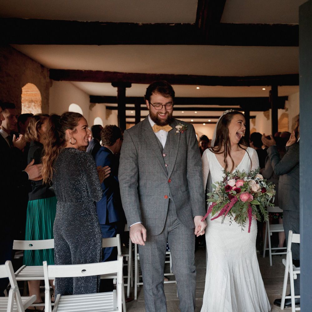 Bride and groom walking down the aisle together - bride smiling as guests clap
