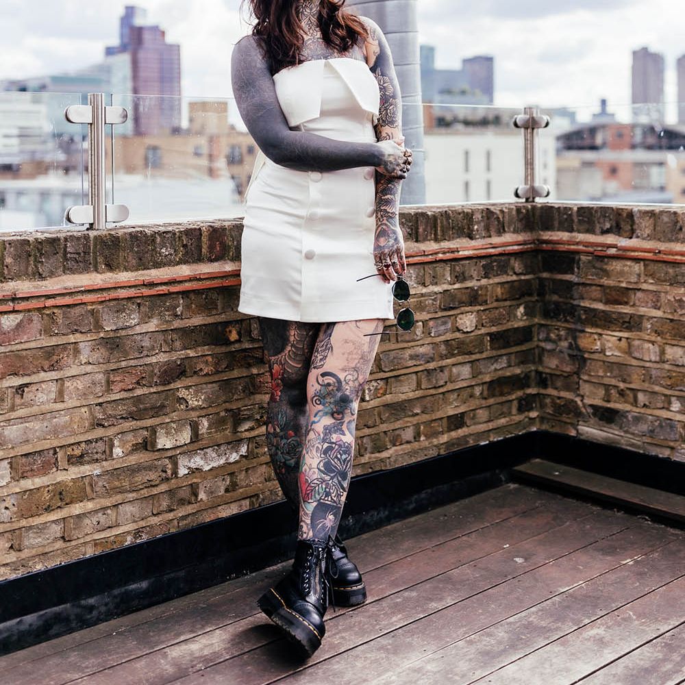 Tattooed bride in a short wedding dress, Dr Marten boots and appliqué headband standing on a roof terrace 