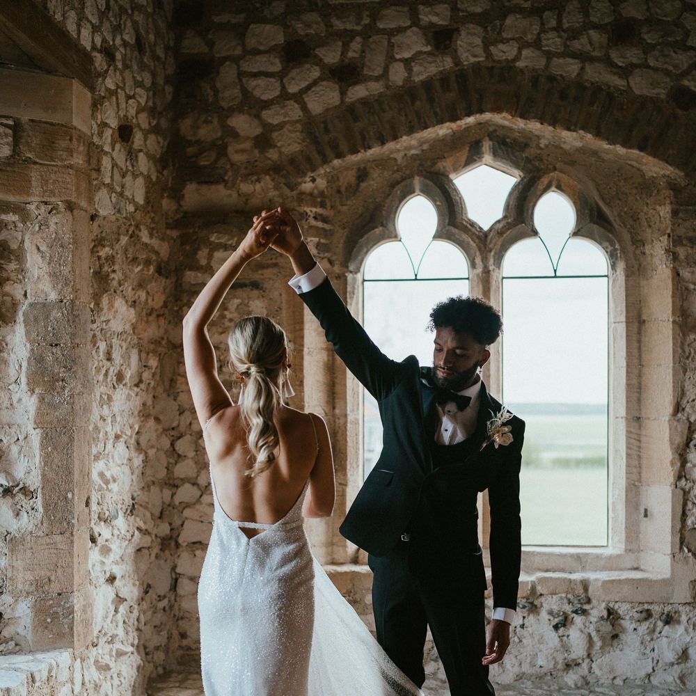Groom in a black tuxedo twirling his bride in a low back Made With Love bridal gown 