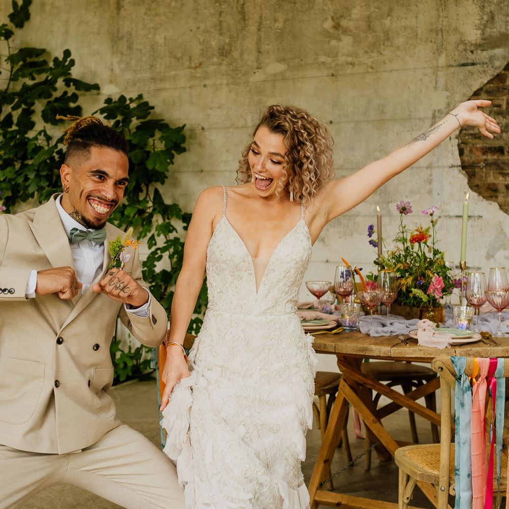 Bride in a fitted wedding dress with straps and groom in a beige suit celebrating at their colourful fiesta theme wedding 