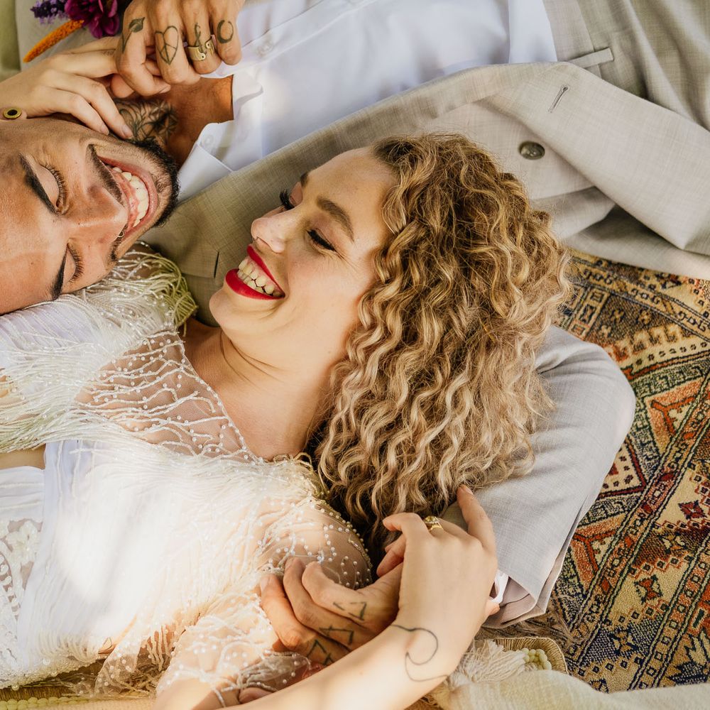 Blonde curly haired bride with bright red lipstick laying on wool rugs with her groom at their fiesta theme wedding 