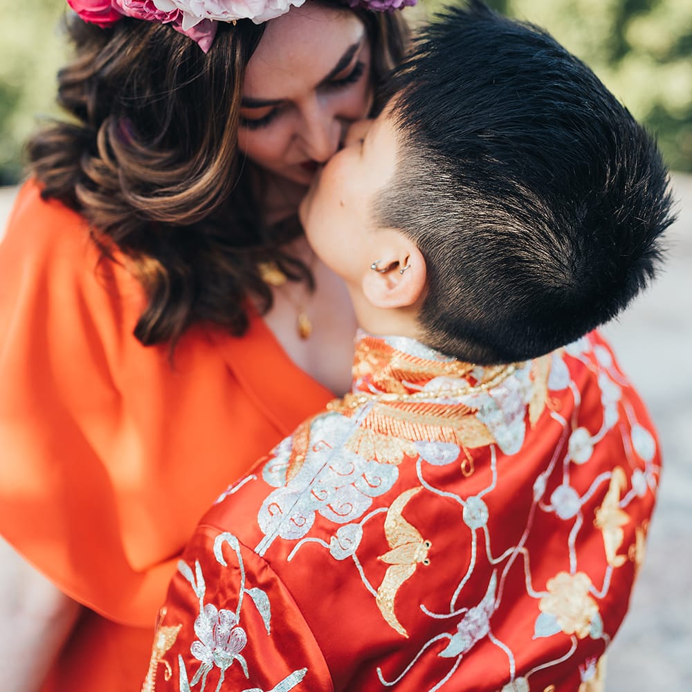 Brides kiss on their wedding day as bride wears pink floral crown