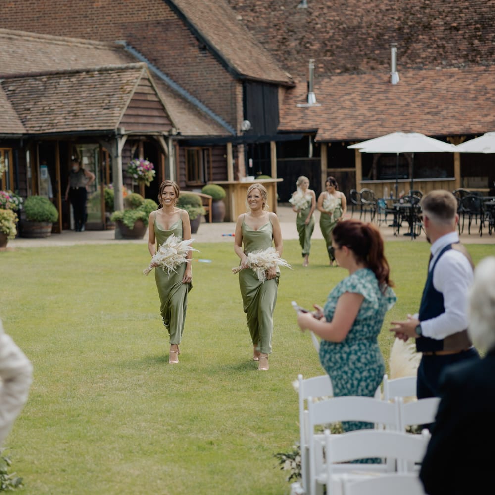 Bridesmaids in green satin dresses walking down the aisle at outdoor wedding ceremony at Cooling Castle Barn 