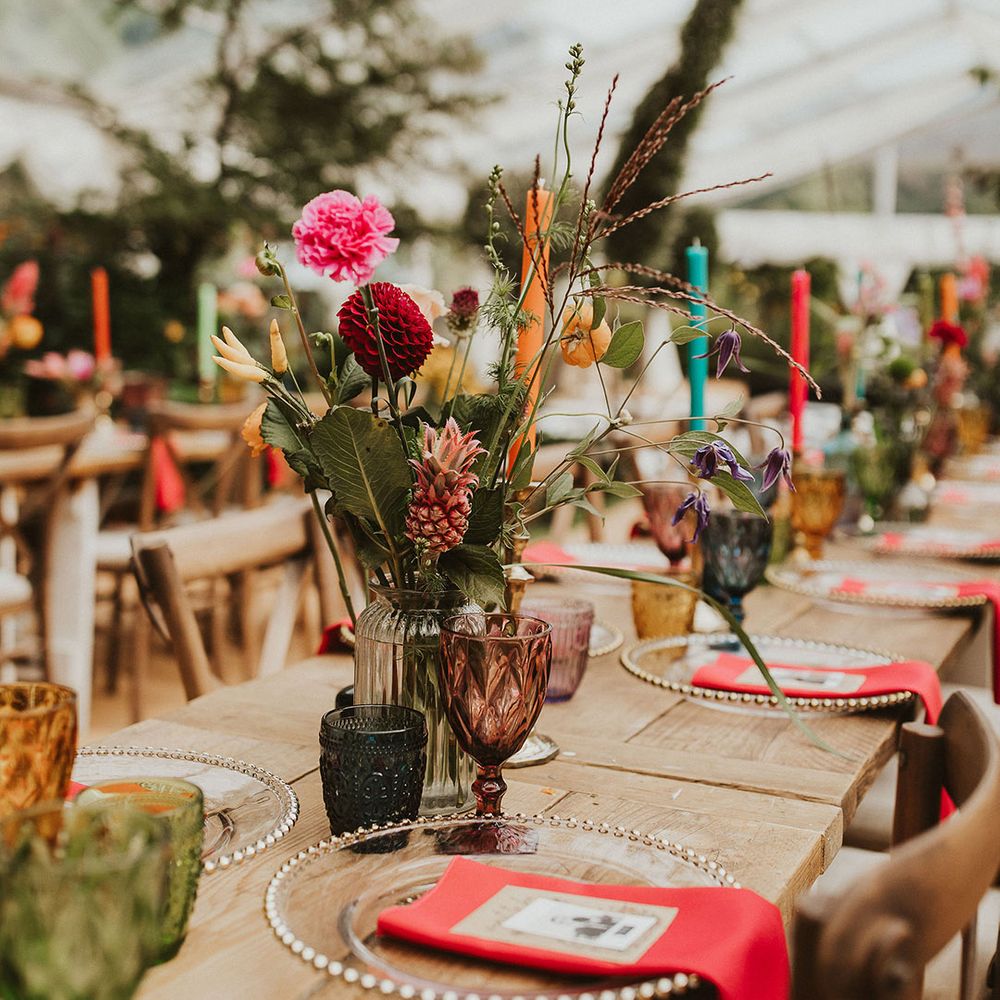 Bright wedding table decor with flower stems in bottles, coloured goblets and glass charger plates 