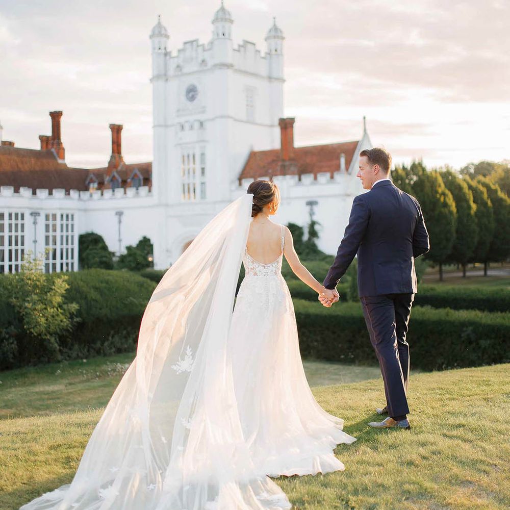 Bride & groom walk across the grounds of Danesfield house as the brides veil blows in the wind