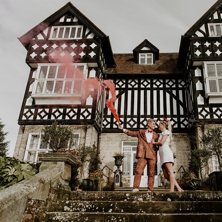 Bride in a leopard print trouser suit holding a smoke flare at fun LGBTQ+ wedding at The Highfield House, Yorkshire 