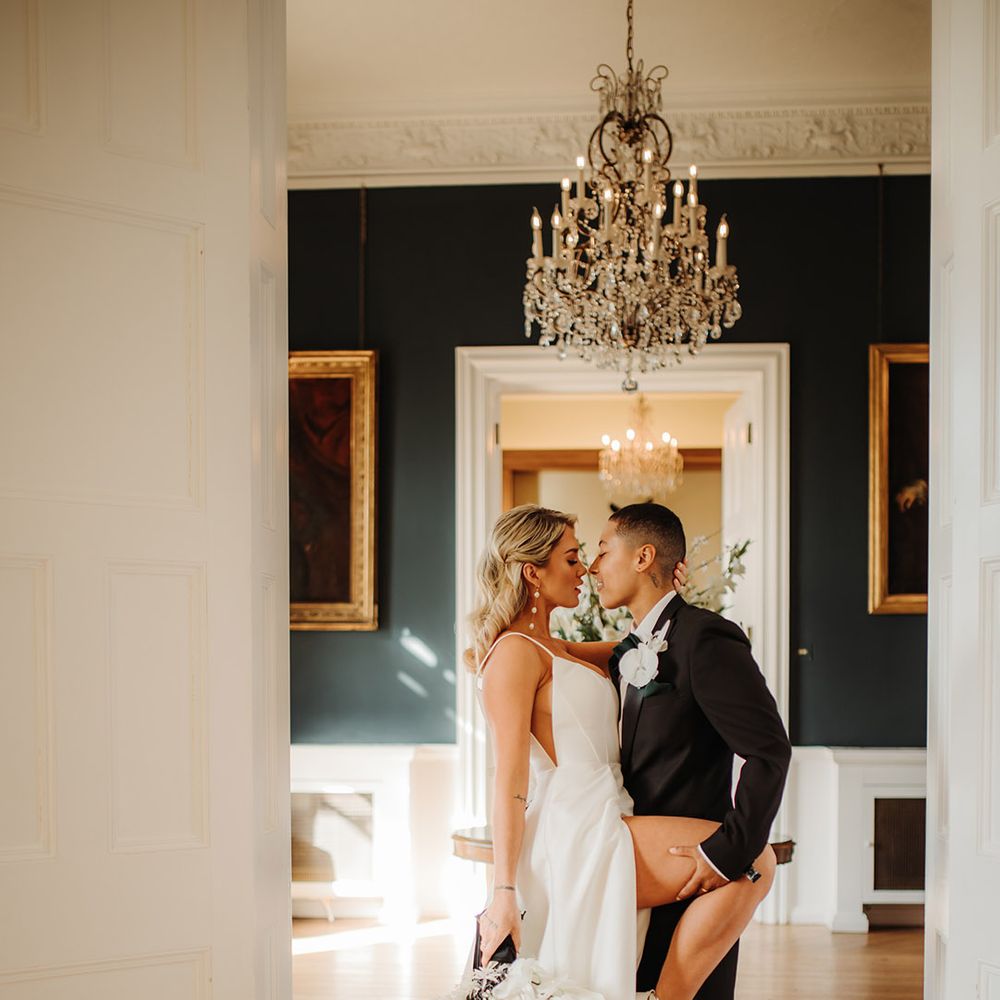 Bride in a princess wedidng dress with side slit holding her leg up for her partner to hold in a tuxedo 