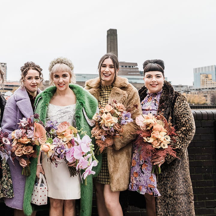 Bride with bridesmaids all in fur coats of different styles and patterns holding purple and orange wedding bouquets