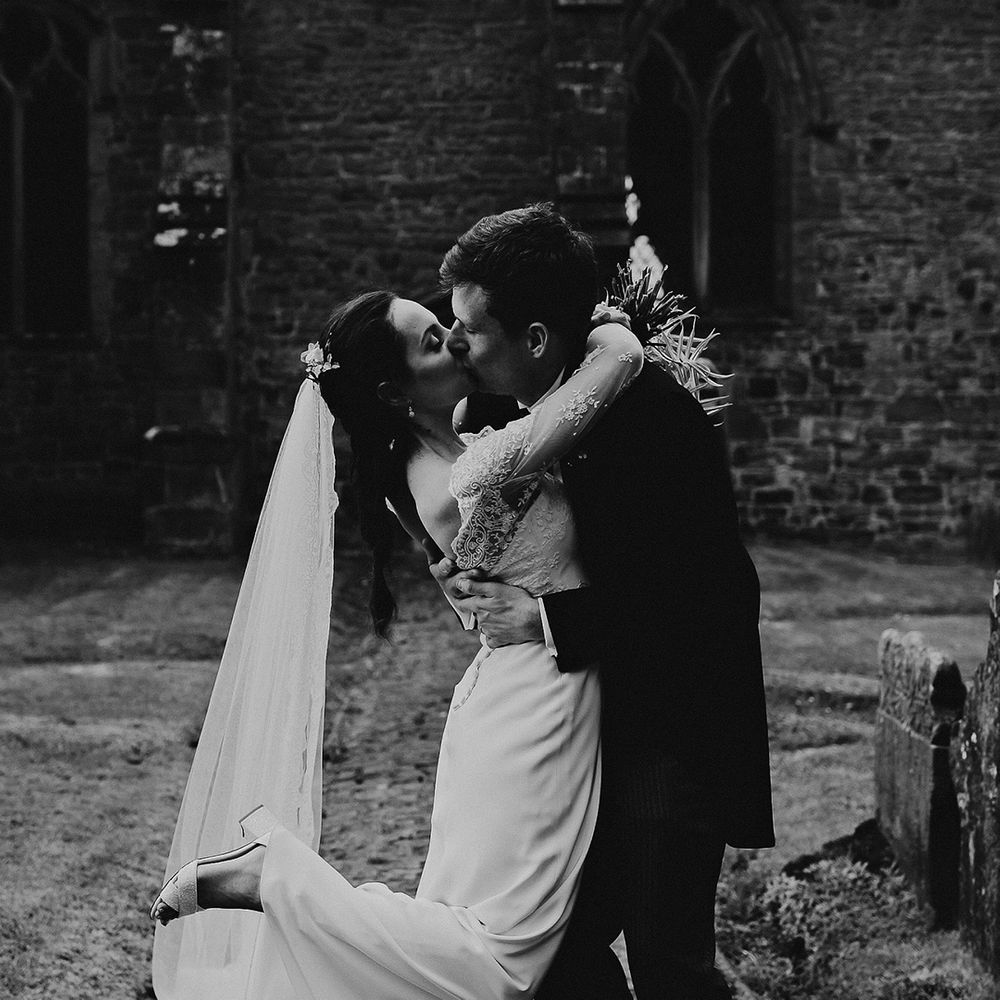 Bride in satin and lace wedding dress shoes a kiss with the groom in a black morning suit outside of the church they married in